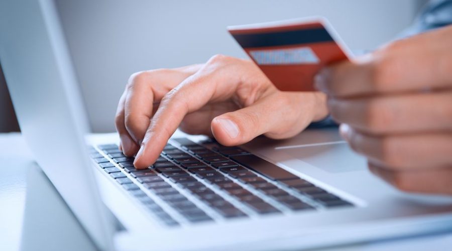 Imagem de uma pessoa usando o computador com um cartão de crédito na mão